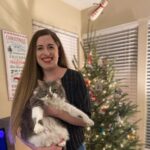 Photo of Carissa Arduini with a gray and white cat, standing in front of a Christmas tree.
